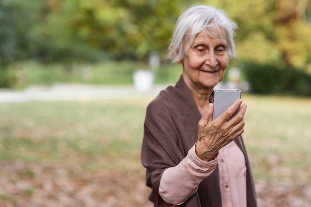 Donna anziana di smiley che tiene smartphone all'aperto con lo spazio della copia
