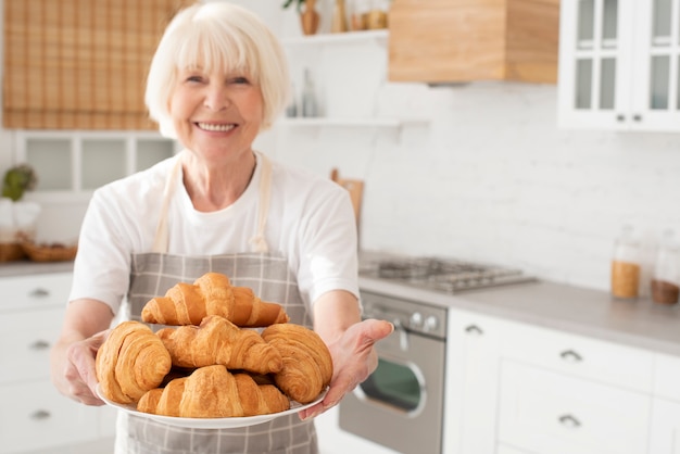 Donna anziana di smiley che tiene una zolla con i croissant