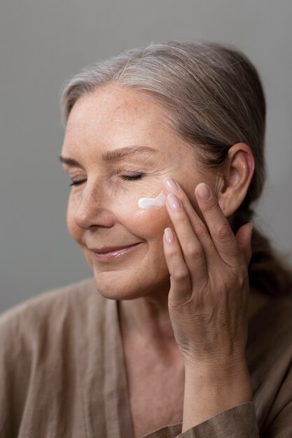 Donna anziana di vista laterale che applica crema per il viso