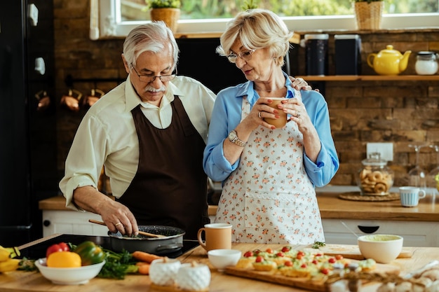 Donna anziana e suo marito che si divertono a cucinare nella loro cucina.