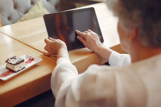 Donna anziana elegante che si siede in un caffè e che per mezzo di un computer portatile