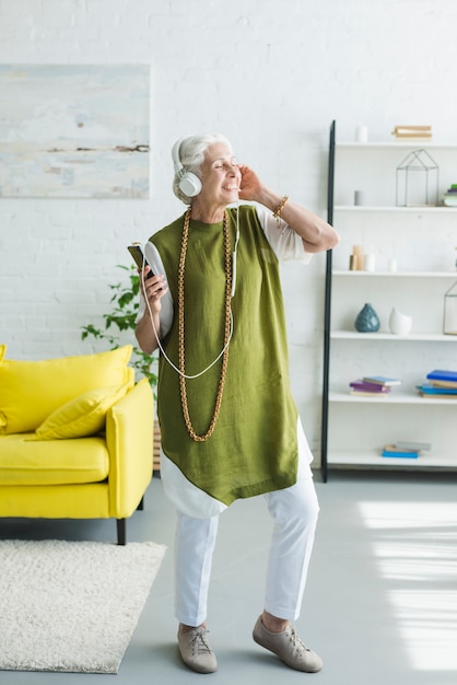 Donna anziana felice che gode della musica sulla cuffia a casa