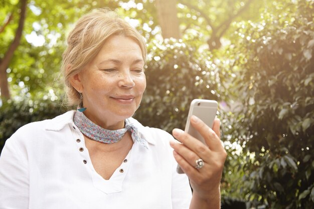 Donna anziana nel parco utilizzando il telefono