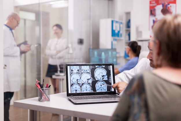 Donna anziana nell'ufficio dell'ospedale che esamina la TAC cerebrale mentre discute con il medico sulla diagnosi. Giovane donna malata e medico anziano con i capelli grigi nel corridoio della clinica.