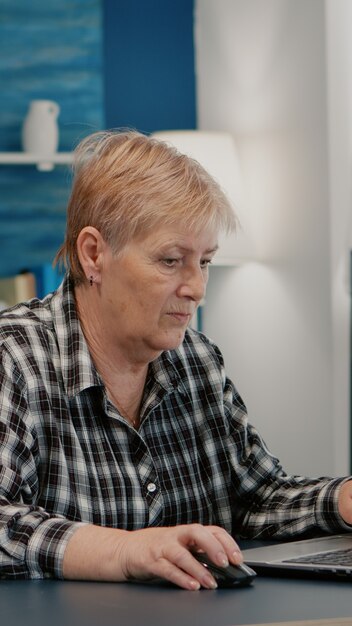 Donna anziana oberata di lavoro che lavora da casa al laptop