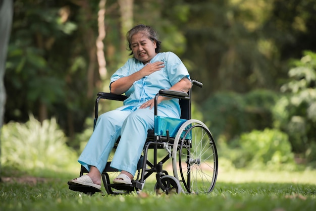 Donna anziana sola che si siede sensibilità triste sulla sedia a rotelle al giardino in ospedale