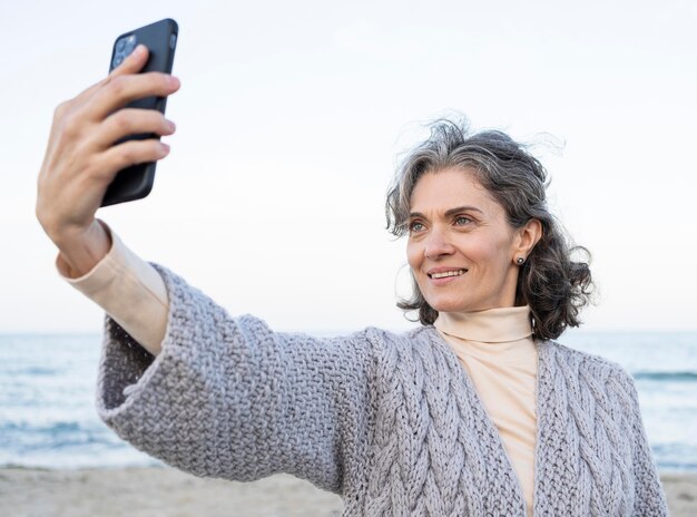 Donna anziana sorridente che si fa un selfie in spiaggia