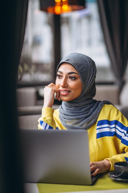 Donna araba in hijab all&#39;interno di un caffè che lavora al computer portatile