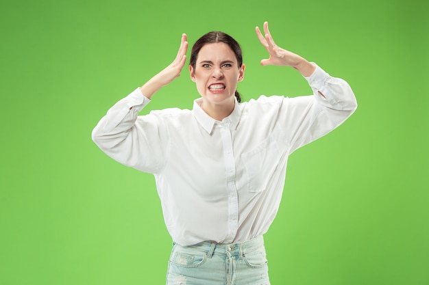 Donna arrabbiata che guarda l'obbiettivo. Donna d'affari aggressiva in piedi isolato su sfondo verde alla moda per studio. Ritratto femminile a mezzo busto. Emozioni umane, concetto di espressione facciale