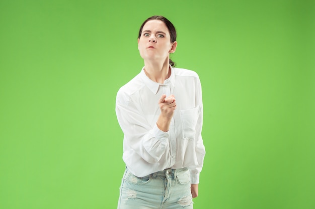 Donna arrabbiata che guarda l'obbiettivo. Donna d'affari aggressiva in piedi isolato su sfondo verde alla moda per studio.