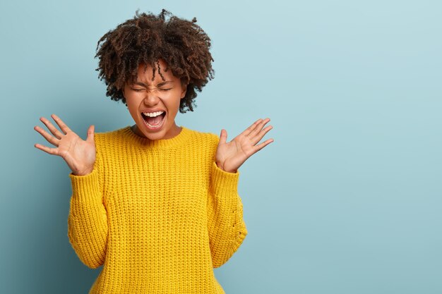 Donna arrabbiata insoddisfatta con un afro che posa in un maglione rosa