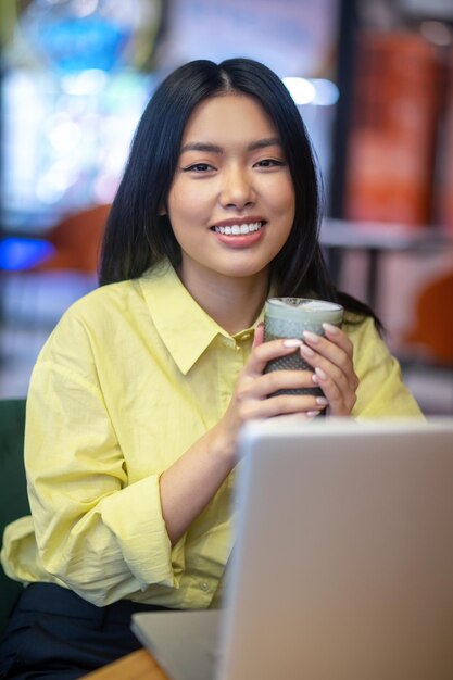 Donna asiatica abbastanza giovane in camicia gialla che lavora ad un computer portatile