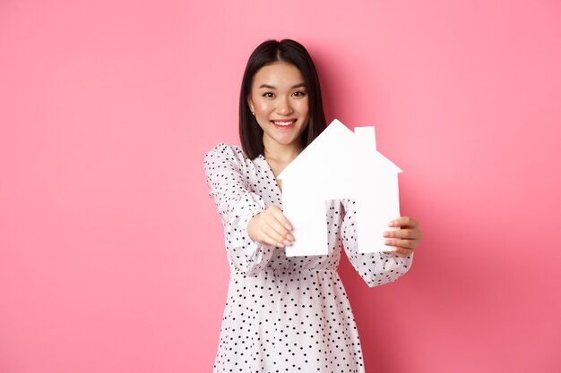 Donna asiatica adulta del settore immobiliare alla ricerca di un modello di casa per la casa e promo sorridente di broker co...