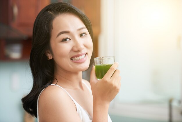 Donna asiatica allegra con bicchiere di succo verde