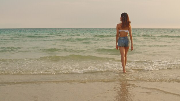 Donna asiatica che cammina sulla spiaggia di sabbia.