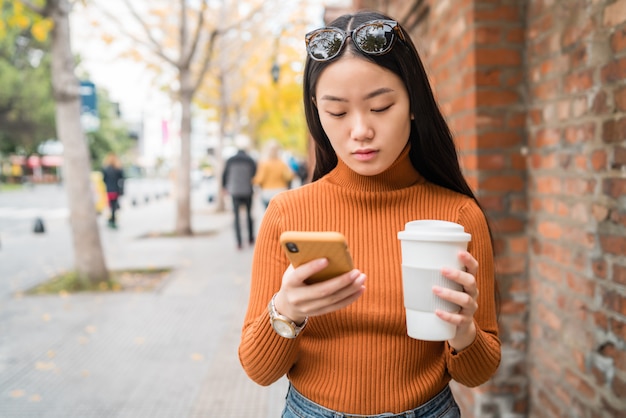 Donna asiatica che per mezzo del suo telefono cellulare.