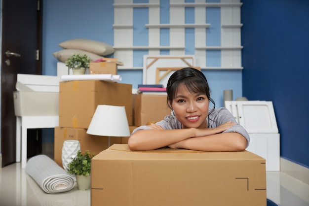 Donna asiatica che riposa la testa sui suoi gomiti e scatola del pacchetto stanco di disimballare nel nuovo appartamento