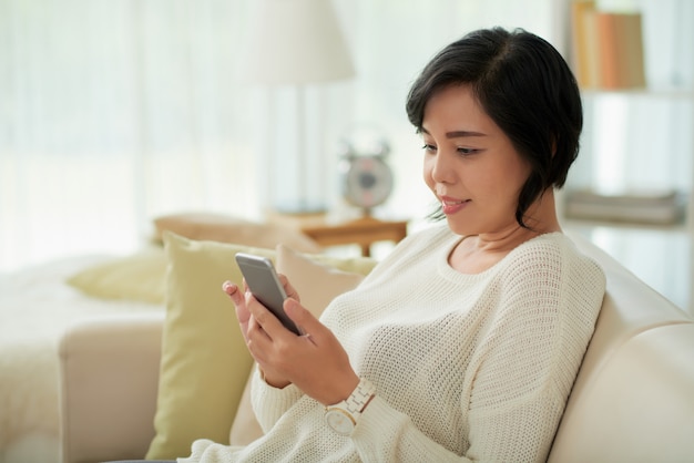 Donna asiatica che si rilassa a casa facendo uso dello smartphone