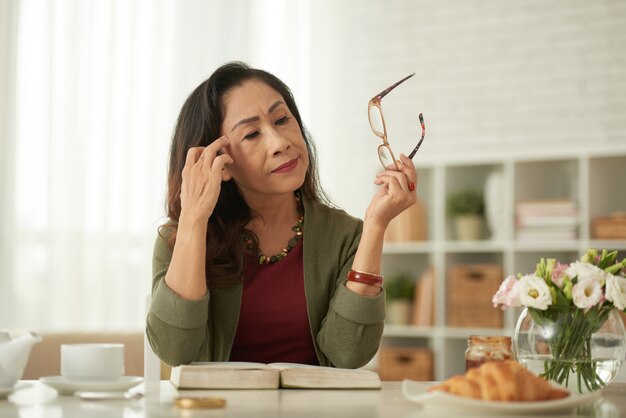 Donna asiatica che toglie gli occhiali che si siedono alla tavola nella mattina