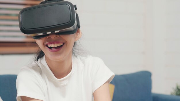 Donna asiatica dell&#39;adolescente che utilizza il simulatore di realtà virtuale di vetro che gioca i video giochi in salone
