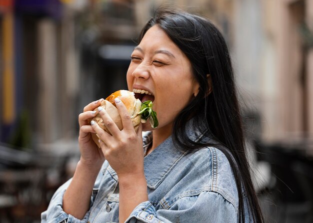 Donna asiatica felice che mangia un hamburger all'aperto