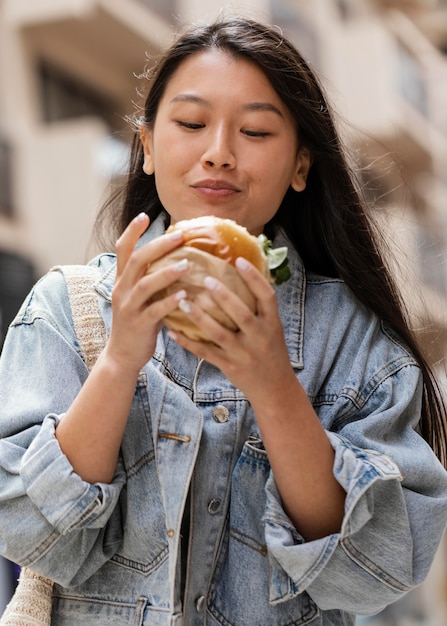 Donna asiatica felice che mangia un hamburger all'aperto