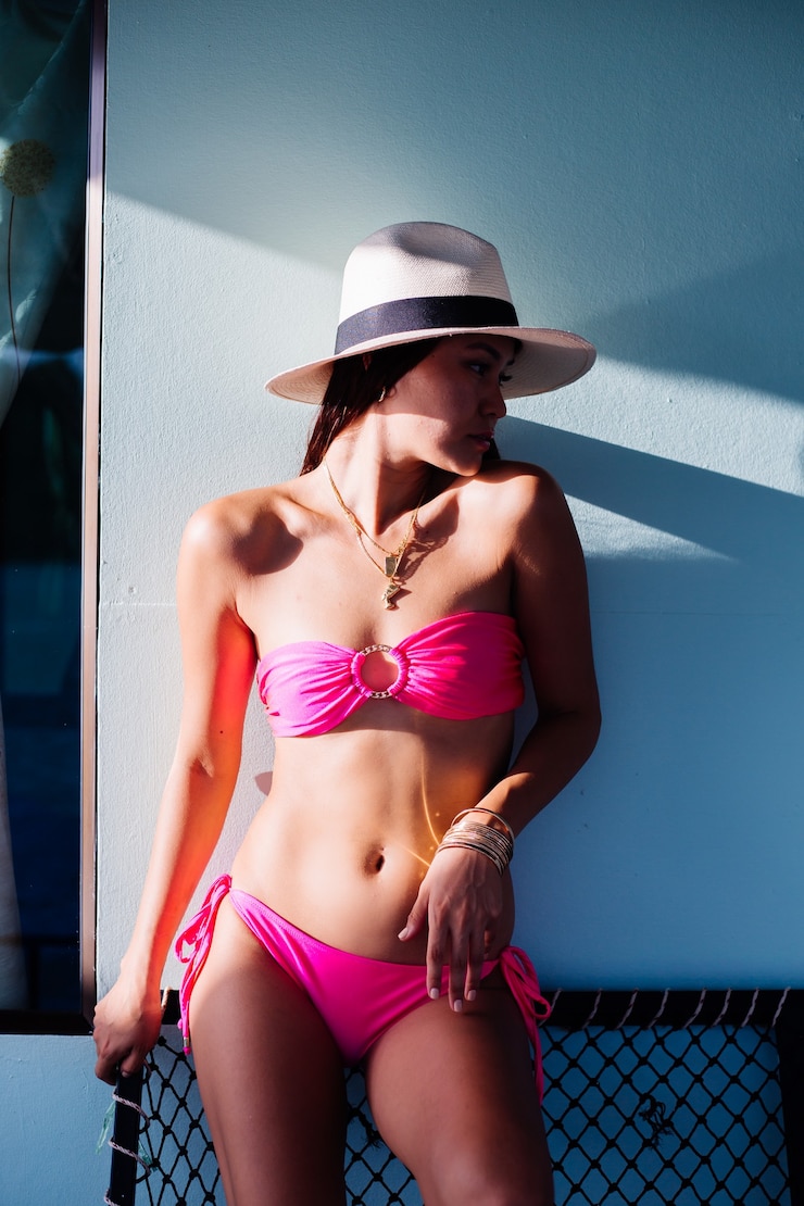 Foto gratuito donna asiatica in bikini rosa si trova fuori casa sul muro blu