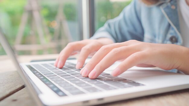 Donna asiatica indipendente di affari che lavora, facendo progetti e inviando email sul computer portatile o sul computer mentre sedendosi sulla tavola in caffè.