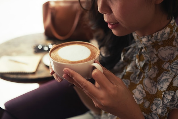 Donna asiatica irriconoscibile che tiene tazza di cappuccino in caffè