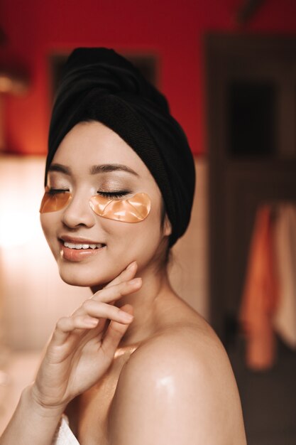 Donna asiatica senza trucco in posa in un asciugamano e con macchie d'oro per gli occhi