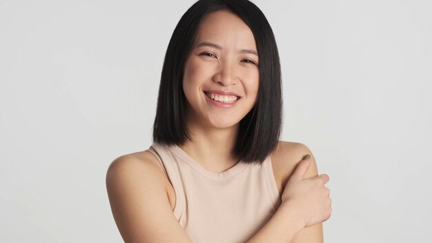 Donna asiatica sinceramente sorridente alla telecamera cercando così felice isolato su sfondo bianco Ragazza asiatica allegra