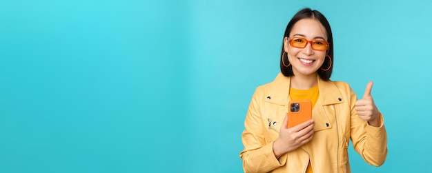 Donna asiatica sorridente che mostra i pollici in su registrando sul telefono cellulare utilizzando l'app per smartphone e la raccomandazione