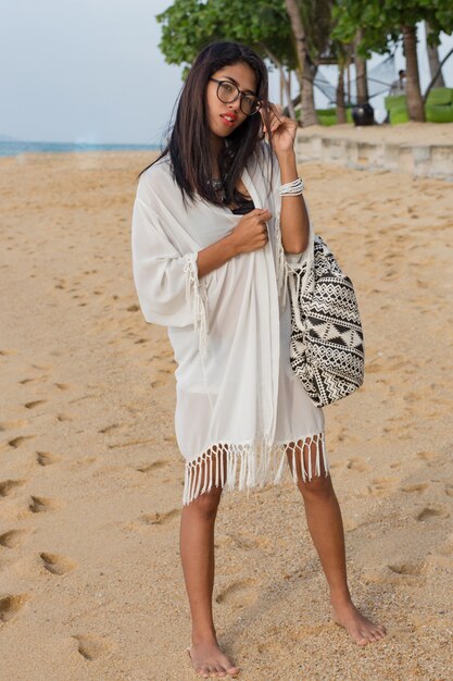 Donna asiatica sveglia del viaggiatore in vestito bianco che cammina sulla spiaggia tropicale. Bella donna che gode delle vacanze