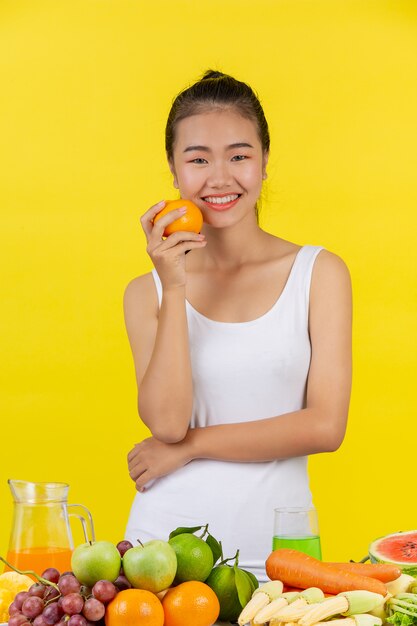 Donna asiatica Tieni le arance con la mano destra e sul tavolo ci sono molti frutti.