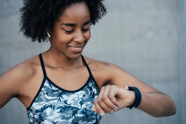 Donna atletica afro che controlla il tempo sul suo orologio intelligente mentre si allena all'aperto