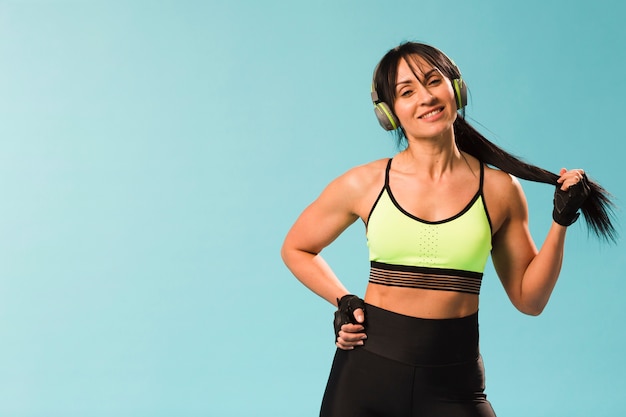 Donna atletica di smiley che posa in attrezzatura della palestra con le cuffie