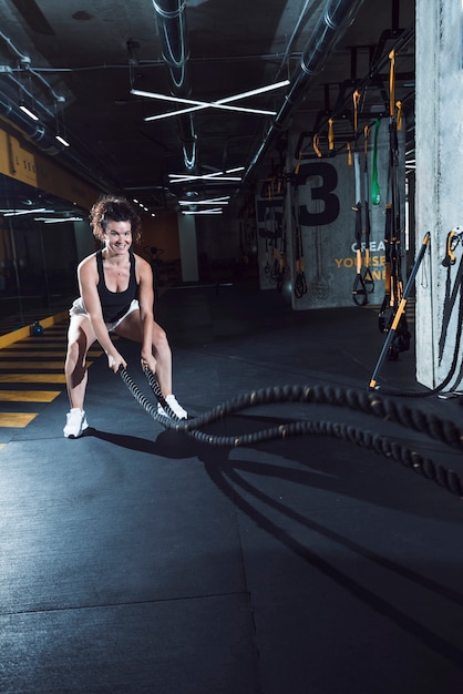 Donna atletica felice che si esercita con le corde di battaglia in palestra