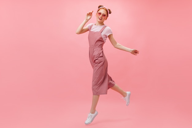 Donna attiva in tuta rosa, t-shirt e occhiali alla moda si muove su sfondo rosa.