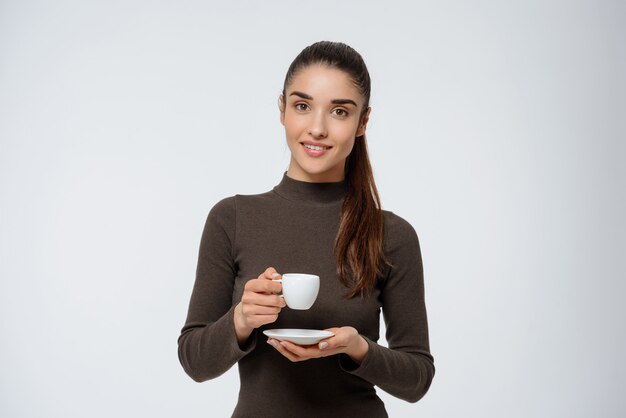 Donna attraente che beve caffè, tenendo la tazza di caffè espresso