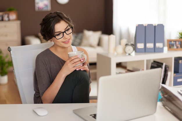 Donna attraente che osserva sul computer portatile mentre beve il caffè a casa