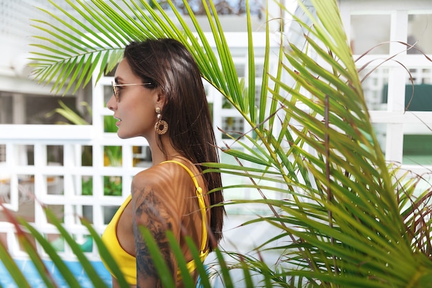 Donna attraente con una splendida abbronzatura posa vicino alla piscina al popolare.