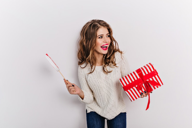 Foto gratuito donna attraente di aspetto adorabile, che indossa un top bianco caldo e jeans mamma che tengono regalo di natale. ritratto di sorridente modello dai capelli lunghi