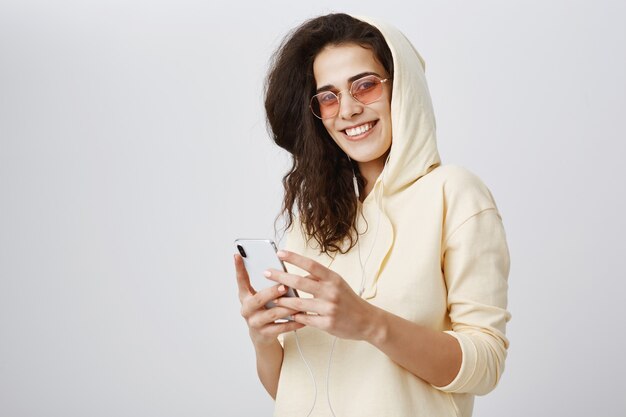 Donna attraente in occhiali da sole utilizzando smartphone e sorridente