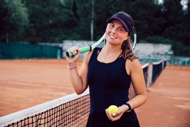 Donna attraente sorridente in abiti sportivi, in piedi sul campo con la racchetta da tennis