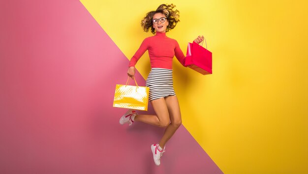 Donna attraente sorridente in vestito colorato alla moda che salta con le borse della spesa