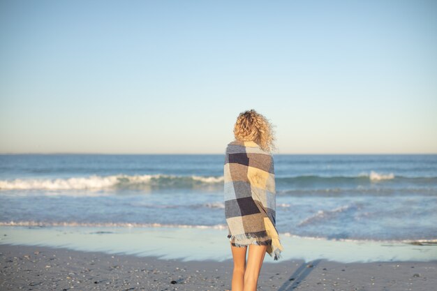 Donna avvolta in una coperta in piedi sulla spiaggia