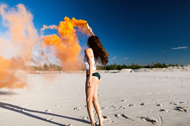 Donna balla con il fumo arancione sulla spiaggia bianca sotto il cielo blu