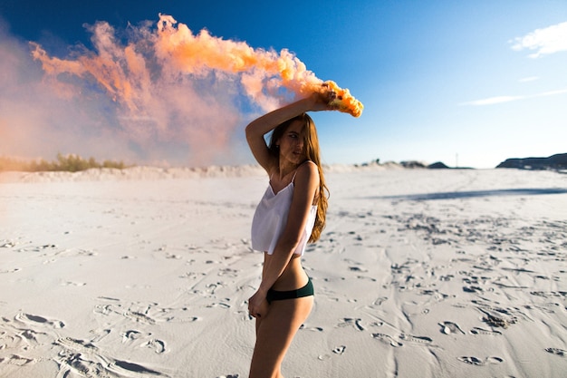 Donna balla con il fumo arancione sulla spiaggia bianca sotto il cielo blu