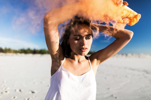 Donna balla con il fumo arancione sulla spiaggia bianca sotto il cielo blu