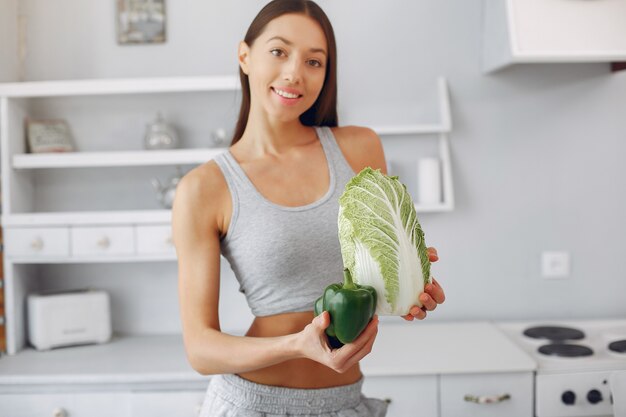 Donna bella e sportiva in una cucina con verdure